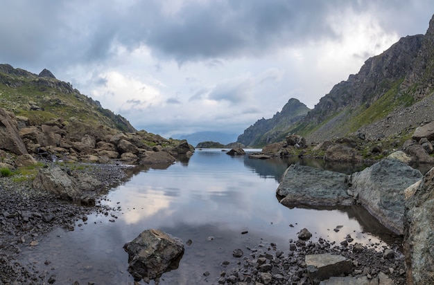 Paisagem panorama com um lago nas montanhas, enormes pedras e pedras na costa e reflexo das nuvens