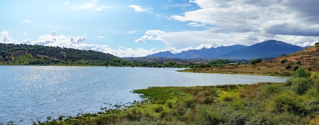 Paisagem panorâmica de montanha com grande lago ensolarado e pequena cidade na costa.