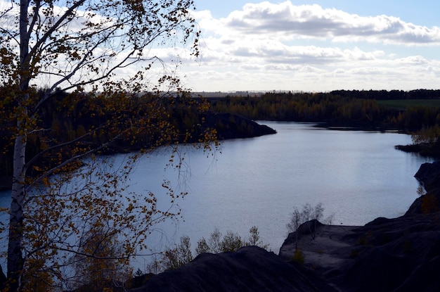 Paisagem panorâmica natural do sol com um lago, árvores amarelas, céu azul nublado e montanhas de carvão