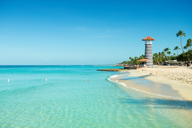 Paisagem paradisíaca do caribe. mar límpido, areia branca, palmeiras tropicais e farol na costa arenosa