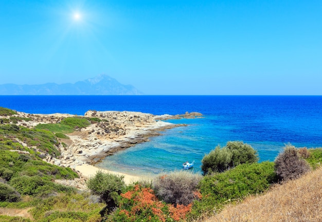 Paisagem pedregosa da costa do mar do sol de verão com vista de montagem de Athos em distante (Halkidiki, Sithonia, Grécia).