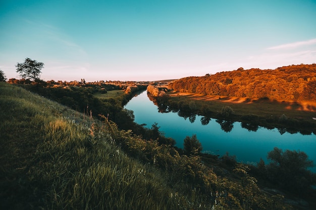 Paisagem pitoresca perto da cidade com a grama do pôr do sol e o rio azul