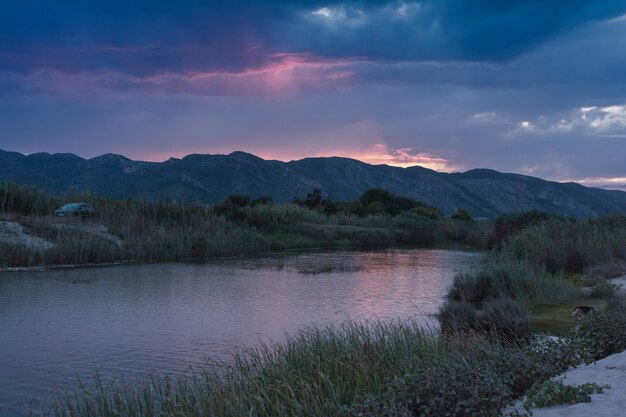 paisagem praia de montanha ao longo do rio ao pôr do sol com céu roxo n xeraco, valencia