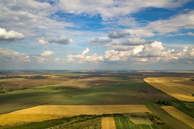 Paisagem rural aérea com campos de agricultura remendados amarelo e céu azul com nuvens brancas.