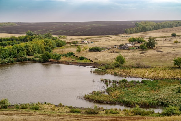 Paisagem rural com aldeia nas margens da lagoa e campos Rússia Orenburg região fazenda Arapovka