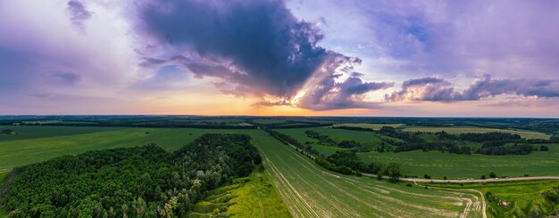 Paisagem rural do pôr do sol de verão com campos verdes e panorama de vista aérea de fundo natural do céu colorido dramático