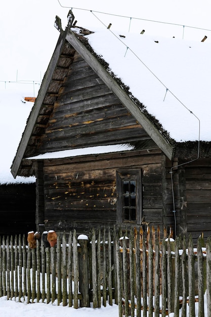 Paisagem russa de inverno Uma velha cabana de madeira uma casa de madeira com telhado de palha Vila russa abandonada coberta de neve Casa de madeira com um celeiro com uma cerca de vime de madeira