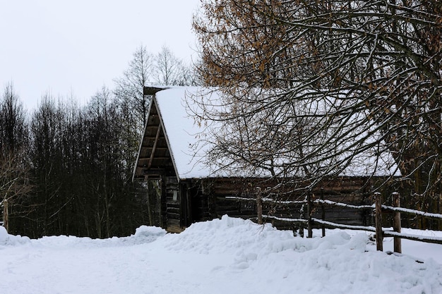 Paisagem russa de inverno Uma velha cabana de madeira uma casa de madeira com telhado de palha Vila russa abandonada coberta de neve Casa de madeira com um celeiro com uma cerca de vime de madeira