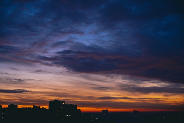 Foto paisagem urbana com amanhecer quente vívido. céu dramático violeta azul dramático surpreendente acima das silhuetas escuras dos edifícios da cidade. luz do sol laranja. fundo atmosférico do nascer do sol em tempo nublado. copie o espaço.