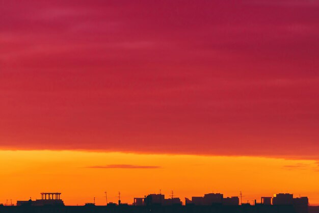 Paisagem urbana com amanhecer surrealista vívido. Incrível quente céu nublado dramático acima silhuetas escuras dos edifícios da cidade.