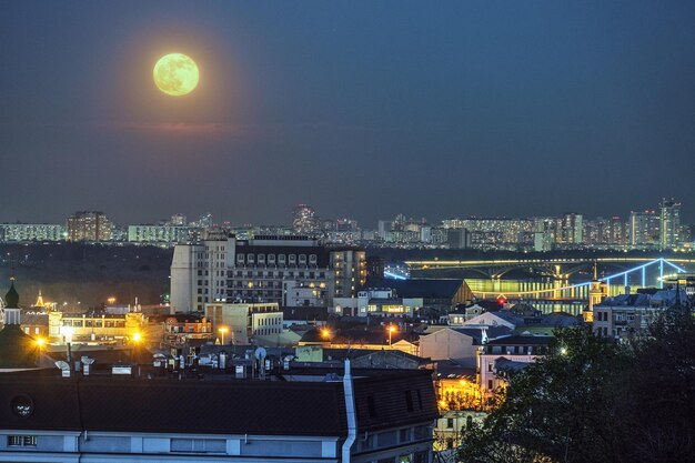 Paisagem urbana noturna com grande lua cheia sobre Podil Kyiv nas luzes da cidade da Ucrânia e vista para a ponte