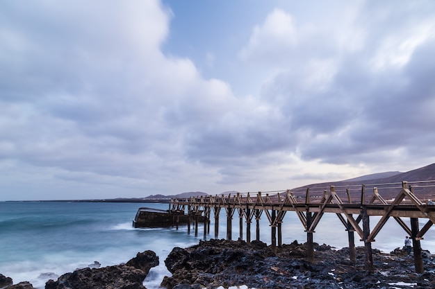 Paisaje al atardecer con puente en la playa, con cielo nublado en lanzarote canarias