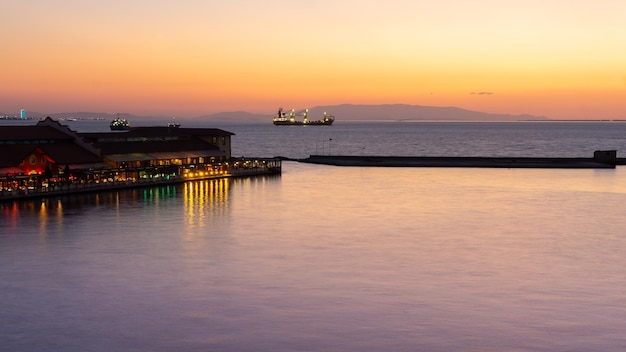 Paisaje al atardecer del puerto de Izmir en Turquía con la silueta de los barcos navegando y las montañas al fondo en formato horizontal