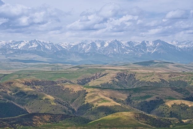 Paisaje alpino atmosférico con cordillera y colinas verdes bajo un cielo nublado espectacular