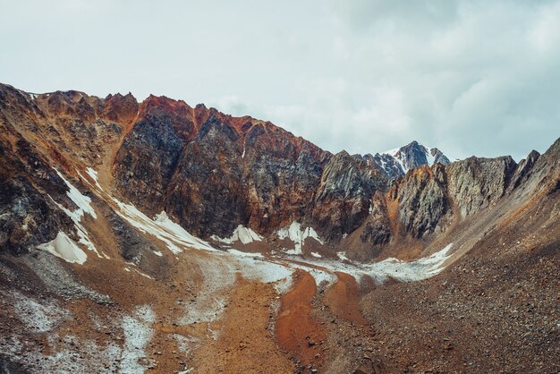 Paisaje alpino atmosférico con grandes rocosas y una lengua glaciar inusual cubierta de piedras. Hermosa pared puntiaguda de la montaña rocosa. Maravilloso paisaje montañoso vívido con lengua glacial. Tonos terrestres.