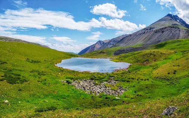 Paisaje alpino azul verde brillante con lago de montaña en el valle de las tierras altas en la luz del sol y la gran montaña bajo un cielo nublado azul. Sombra de nubes en el valle de la montaña verde. Vistas panorámicas.