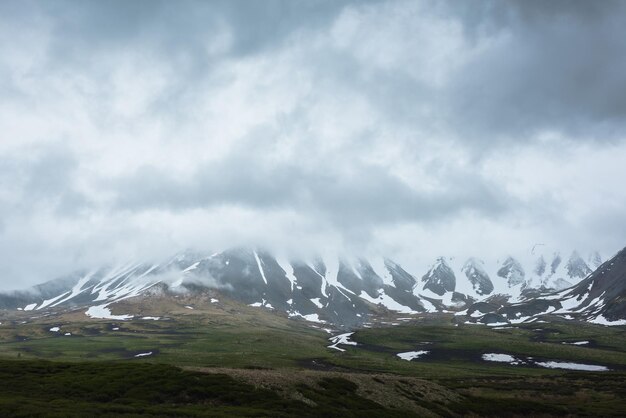 Foto paisaje alpino dramático con montañas nevadas en nubes grises bajas paisaje atmosférico sombrío de la tundra bajo un cielo gris plomo vista minimalista sombría de la cordillera entre nubes lluviosas bajas en nubes cubiertas