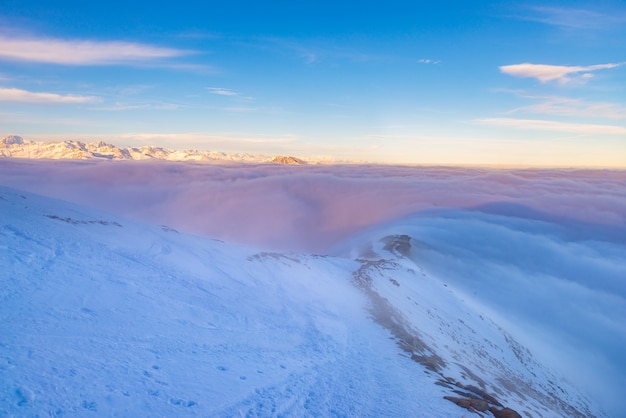 Paisaje alpino escénico, nubes en el valle arisign picos de las montañas luz del atardecer, nieve del invierno.