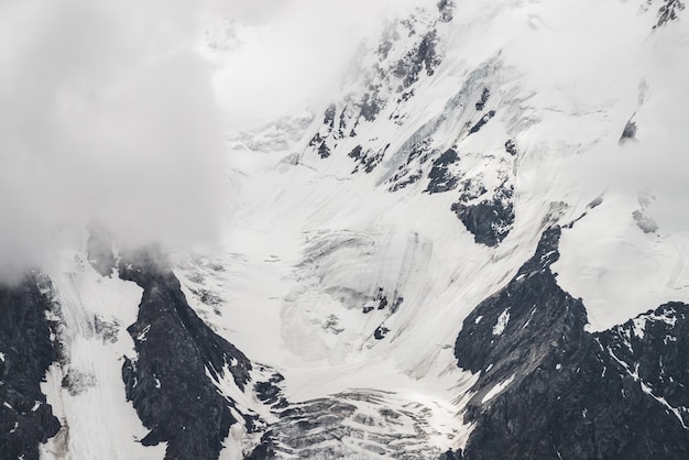 Paisaje alpino con textura minimalista atmosférica con glaciar masivo en la gran montaña en nubes bajas. montaña nevada Grietas en el hielo. Majestuoso paisaje brumoso brumoso en gran altitud.