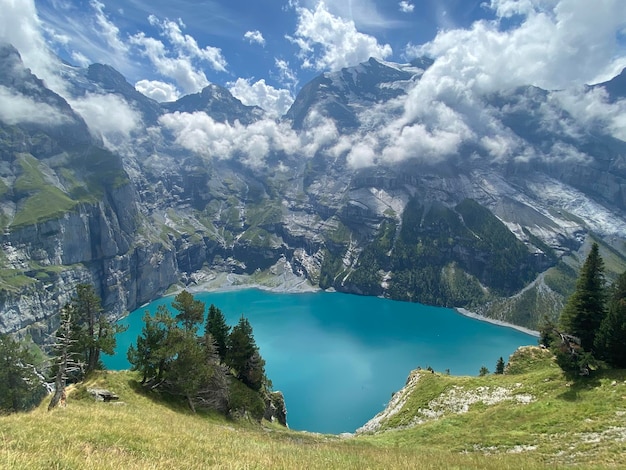 paisaje de alta montaña con lago azul, pinos y nubes.