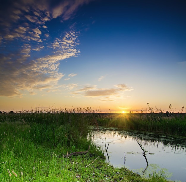 Paisaje de amanecer de verano rural con puente de madera de río y cielo colorido dramático