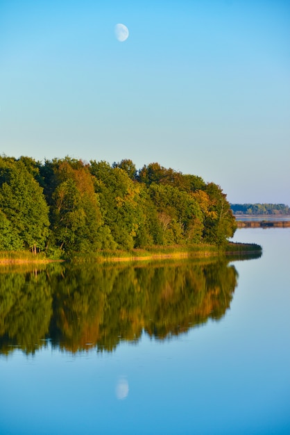 El paisaje de los árboles del bosque amarillo y verde del otoño se refleja en el agua del lago por la tarde