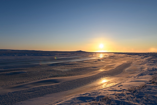 Paisaje ártico en invierno. Pequeño río con hielo en la tundra. Atardecer.