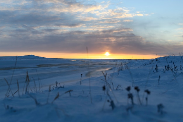 Paisaje ártico en invierno. Pequeño río con hielo en la tundra. Atardecer.