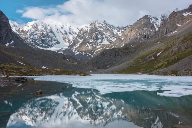 Paisaje atmosférico con lago alpino congelado y altas montañas nevadas El hielo flota en la superficie de agua transparente del lago de montaña Impresionante paisaje con grandes montañas nevadas reflejadas en un lago claro