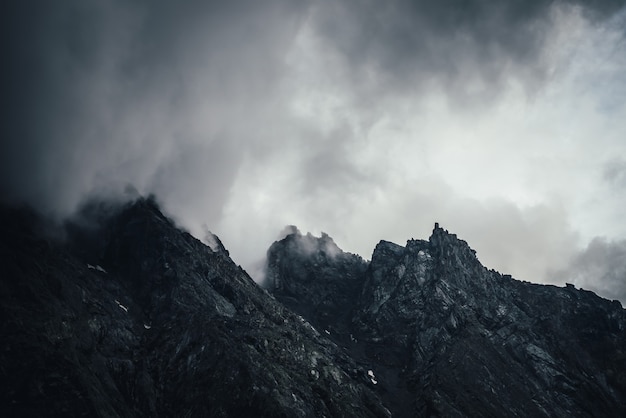 Paisaje atmosférico oscuro con pared de montaña rocosa negra en cielo nublado gris. Nube baja gris en la cima de la montaña negra. Pico de la montaña oscura en nubes bajas en tiempo nublado. Sombrío paisaje minimalista