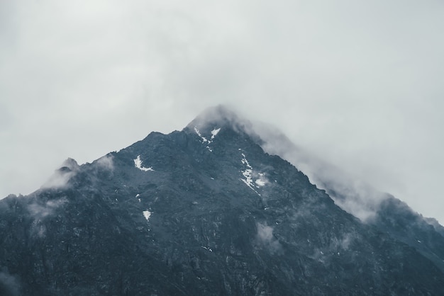 Paisaje atmosférico oscuro con siluetas de montañas negras entre nubes bajas lluviosas. Paisaje de montaña sombrío con nubes de lluvia en la silueta de la cima de la montaña en tiempo nublado. Pico en gris cielo nublado