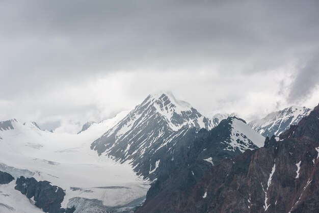 Paisaje atmosférico con rocas afiladas y una alta montaña nevada en nubes bajas lluviosas en un paisaje sombrío dramático con grandes montañas nevadas y glaciares en un cielo nublado gris en tiempo lluvioso