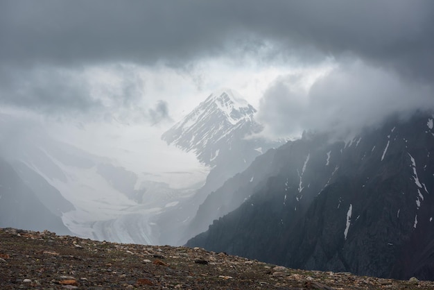 Paisaje atmosférico con siluetas borrosas de rocas afiladas y cima nevada en nubes bajas durante la lluvia Vista espectacular de grandes montañas nevadas y glaciares borrosos en neblina de lluvia en nubes bajas grises