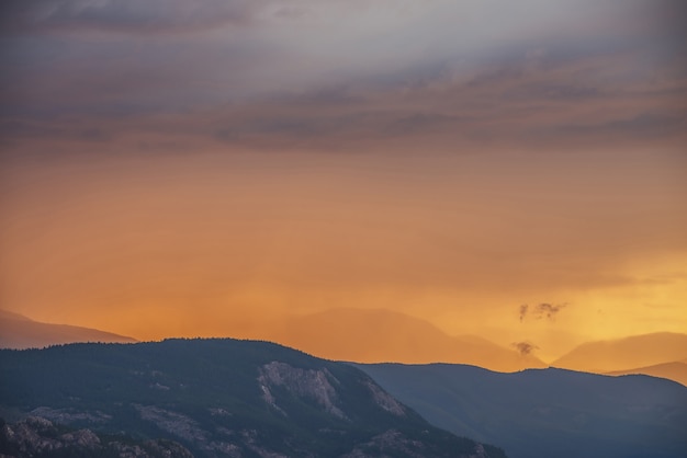 Paisaje atmosférico con siluetas de montañas y bosque sobre roca sobre fondo de cielo anaranjado vivo del amanecer. Paisaje colorido de la naturaleza con puesta de sol o amanecer de color iluminante. Paysage al atardecer.