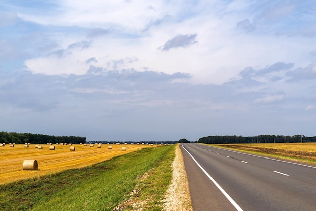 Paisaje del campo agrícola después de la cosecha de cereales con un haz de paja y la carretera