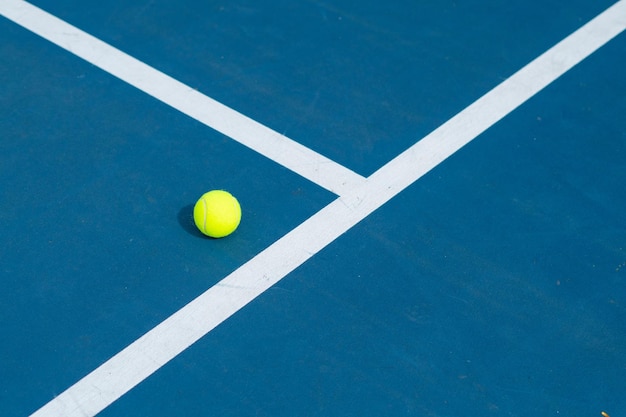 Paisaje de una cancha de tenis azul y verde con una pelota en un día soleado