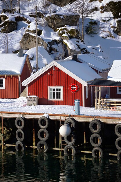 Paisaje - casa de madera tradicional noruega rorbu para estar en la orilla del fiordo y las montañas en la distancia. Noruega.