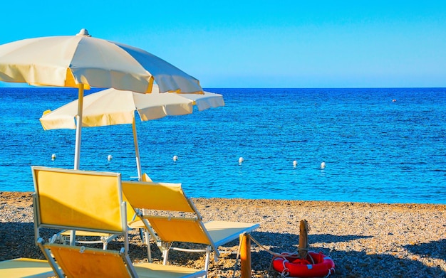 Paisaje de Chia Beach con sombrillas y aguas azules del mar Mediterráneo en la provincia de Cagliari en el sur de Cerdeña en Italia. Paisaje y naturaleza. Técnica mixta.