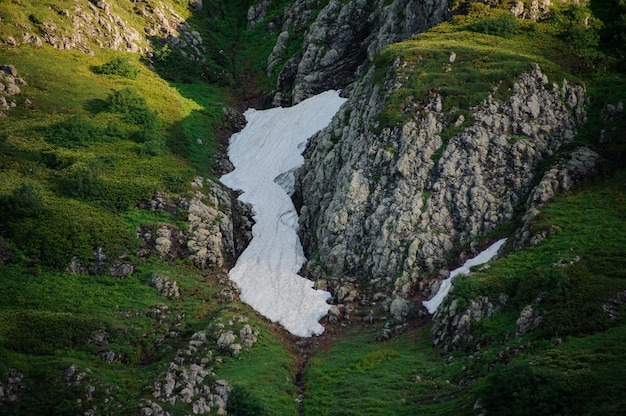 Paisaje de la colina rocosa con hierba con los restos de nieve blanca