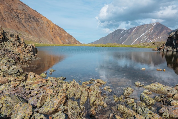 Paisaje colorido con un hermoso lago en un valle de montaña iluminado por el sol entre rocas y una alta montaña bajo un cielo nublado en un clima cambiante Impresionante paisaje con un lago alpino entre piedras a la luz del sol