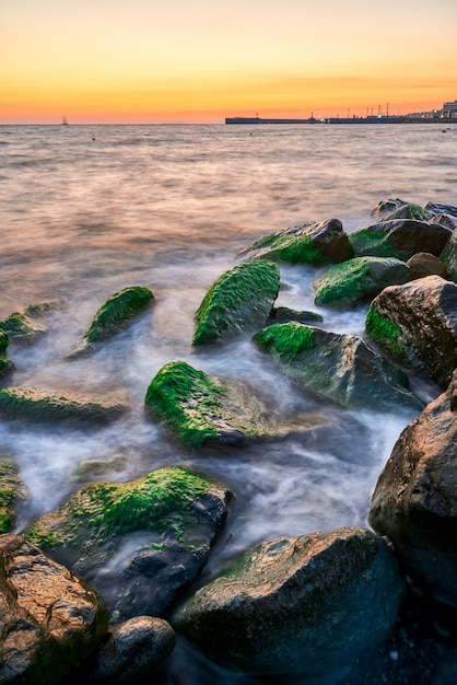 Foto paisaje costero con la cálida luz del atardecer cuando las olas rompen sobre rocas cubiertas de algas