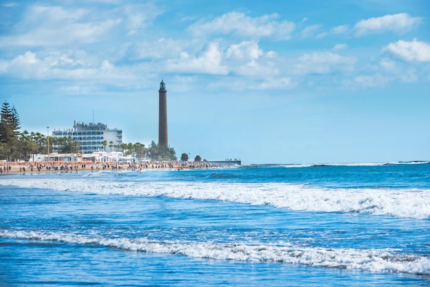 Paisaje costero de la isla de Gran Canaria con playa llena de gente, hotel y faro de Maspalomas. Canarias, España