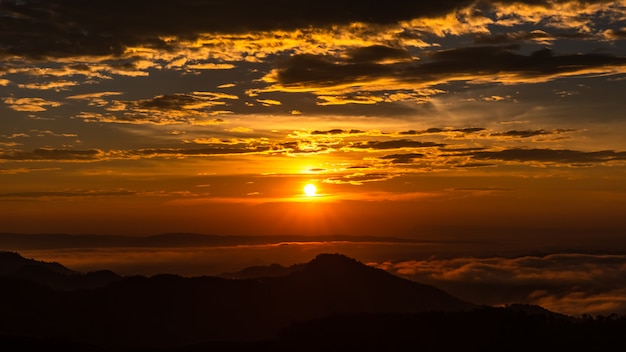 Paisaje crepuscular la puesta de sol y el cielo de nubes con naranja y silueta primer plano de montaña