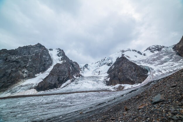 Paisaje dramático con dos cascadas de hielo de glaciar en una gran cordillera de nieve con rocas afiladas bajo un cielo nublado gris Glaciar largo con cascadas De hielo a gran altitud Paisaje sombrío en las montañas en nubes