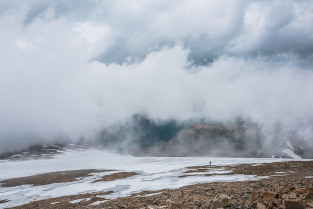 Paisaje dramático con gente dentro de la nube sobre el valle de la montaña abigarrada Turistas en la nube sobre el valle multicolor Nube baja en la colina de piedra con nieve Impresionante paisaje de alta montaña en nubes bajas