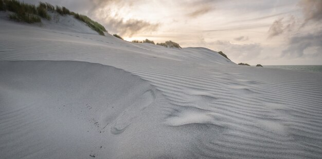 Paisaje de dunas de arena blanca rodada durante la puesta de sol en la playa de wharariki, nueva zelanda