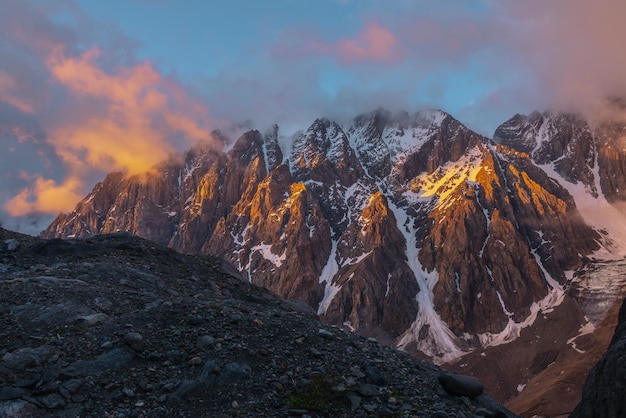 Paisaje escénico con cima de montaña nevada en nubes bajas en colores dorados del amanecer Vista colorida a montañas nevadas y rocas en la luz del sol dorada de la mañana en nubes bajas Impresionante paisaje con rocas doradas