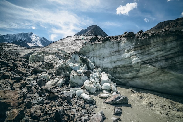 Paisaje escénico con un poderoso río de montaña a partir de un glaciar entre grandes morrenas en el fondo de grandes montañas nevadas. Hermoso paisaje con glaciar en la fuente del turbulento río de montaña.