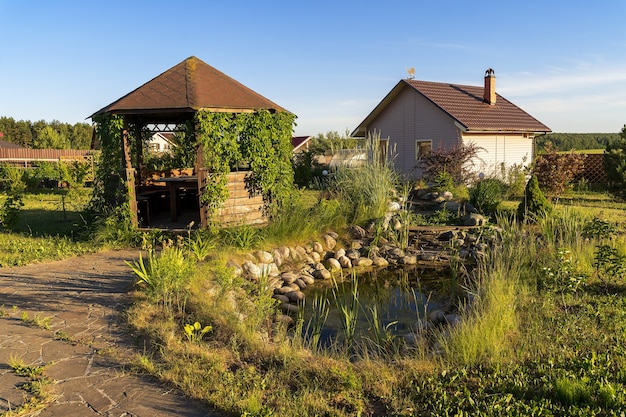 Paisaje con estanque de jardín y pequeña casa de campo en el campo.