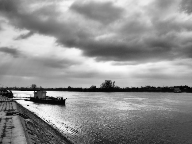 Paisaje fluvial con un barco solitario anclado Clima nublado con nubes pesadas Reflejo de nubes en el agua La orilla opuesta es el horizonte Banco del río Sava de Sremska Mitrovica Serbia
